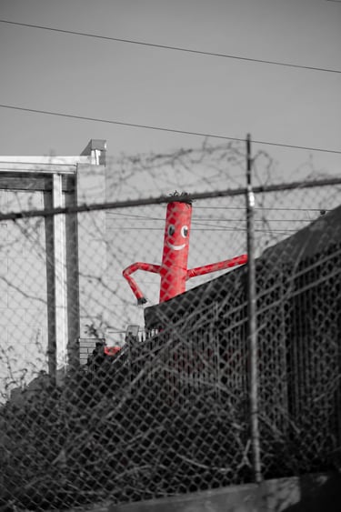 Red inflatable tube man dancer waving behind a chain link fence with barbed wire.