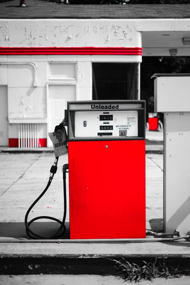 A vintage red unleaded gas pump at an old service station with a sorry out of service sign.