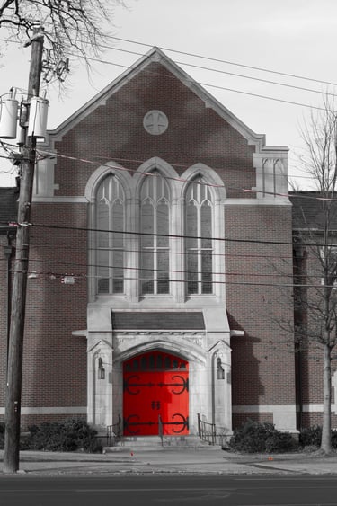 A historic brick church building with a striking bright red front door and arched gothic windows.