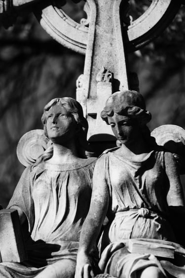 Black and white photo of a vintage stone monument with two carved angel statues at a cemetery.