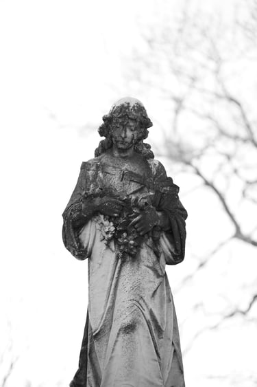 A weathered stone angel cemetery statue holding flowers in a black and white portrait.