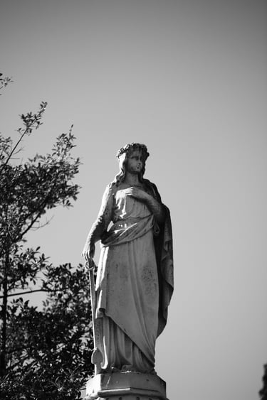 Black and white photo of a vintage stone angel statue in a cemetery against a clear sky.