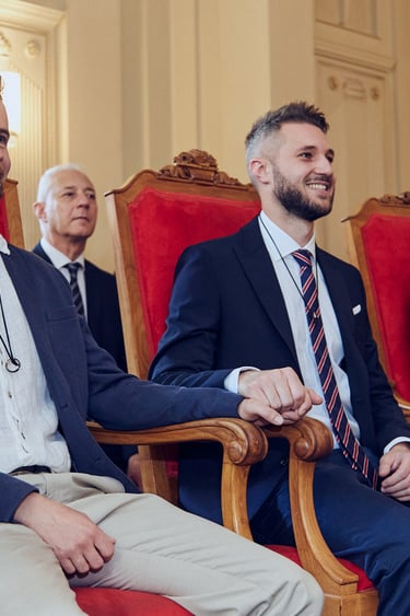 Der Bräutigam sitzt während einer standesamtlichen Trauung auf einem roten Stuhl.