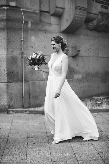 Happy bride walking towards her wedding guests next to a building..
