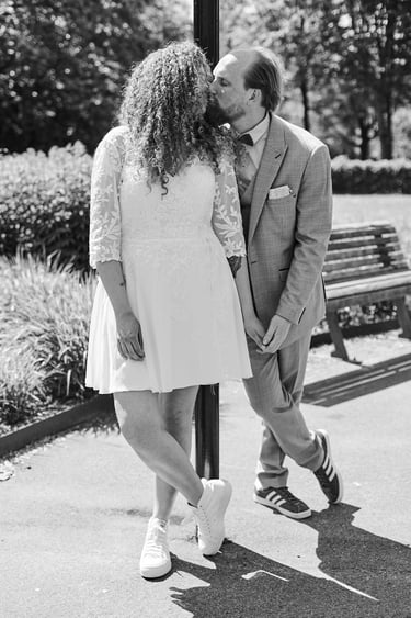 Bride and groom leaning on a pole and kissing.