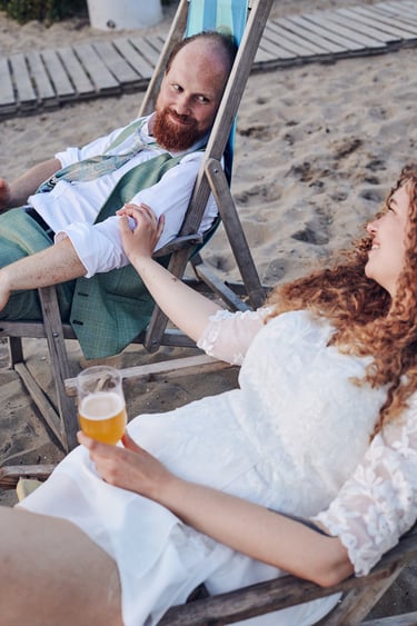 Bride and groom relaxing on deck chairs having a beer.