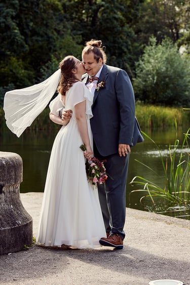 Bride kissing groom on a cheek with her veil floating in the wind.