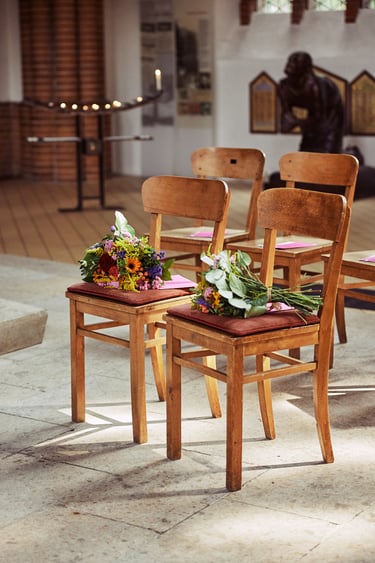 Two chairs in a church with flowers on them.