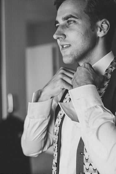 Groom getting ready, tying his tie.