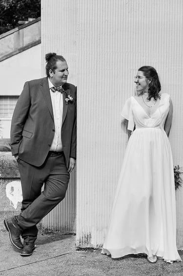 Groom leaning on a wall while looking at his bride.