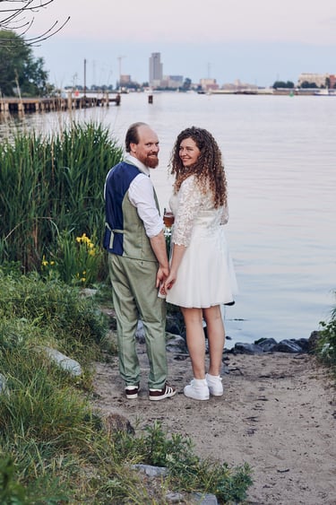 Smiling newlyweds stading at a bank of a river.