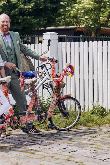 Braut und Bräutigam posieren neben einem Tandemfahrrad neben einem weißen Zaun.
