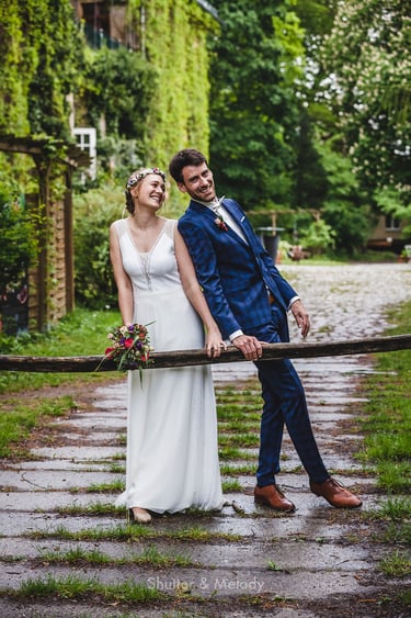 Bride and groom leaning over a wooden barrier.