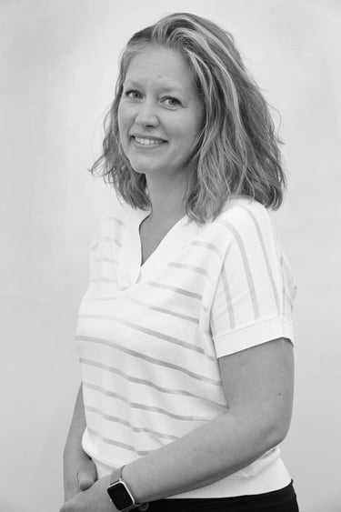 A black and white professional portrait of a smiling woman with wavy hair wearing a striped shirt.