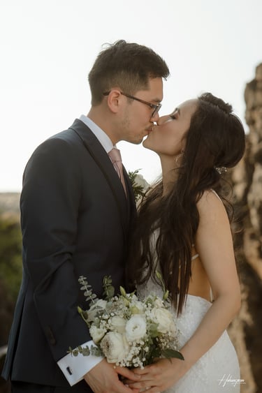 a bride and groom kissing in front of a cliff