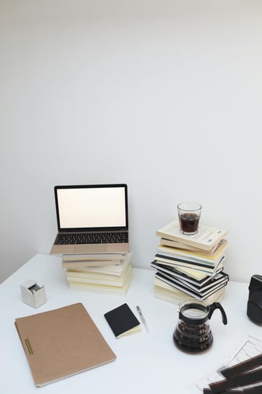 laptop computer with blank screen and piles of books on desk with pot and cup of coffee