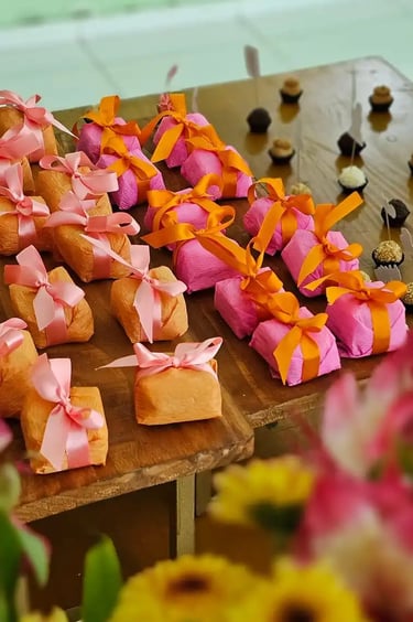 Mesa decorada com doces, incluindo bem-casados embalados em papel colorido e laços vibrantes,