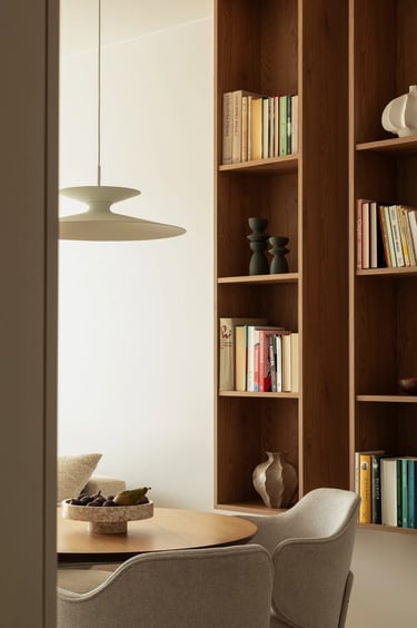 Fotografia wnętrz: okrągły stół, designerska lampa wisząca i dębowy regał na książki.