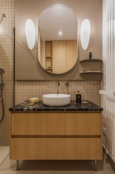 Fotografia wnętrz łazienki: umywalka nablatowa, kamienny blat i beżowe kafelki kwadratowe.