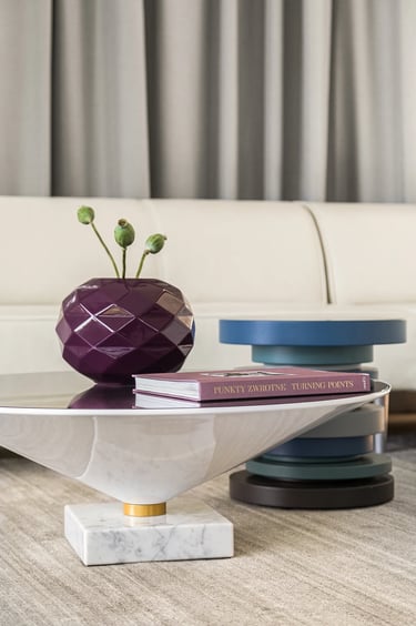 Stylizacja stolika kawowego: fioletowy geometryczny wazon i albumy na marmurowym blacie.