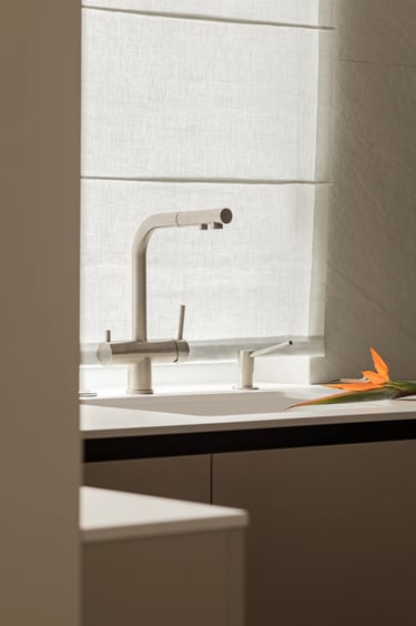 Detal kuchni: bateria stalowa pod oknem, lniana roleta rzymska.