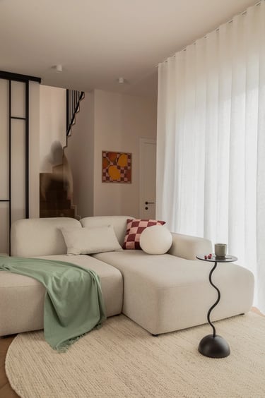 Jasny salon, beżowa sofa bouclé i czarny stolik. Fotografia wnętrz.