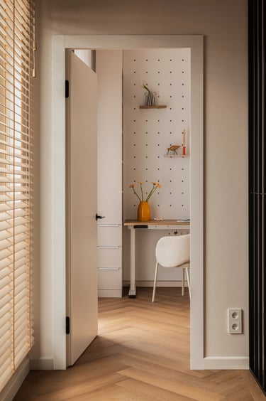 Widok z korytarza na pokój z biurkiem, drewniane żaluzje w oknie.