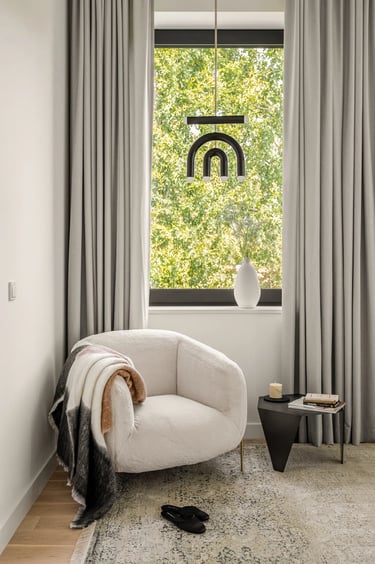Przytulny kącik przy oknie: fotel z tkaniny boucle, czarna lampa wisząca i nowoczesny stolik.