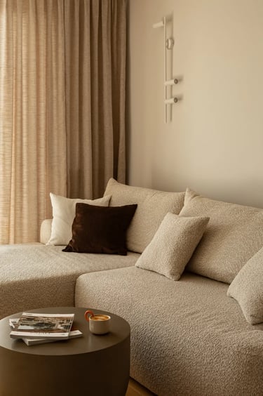 Beżowa narożna sofa boucle i brązowe poduszki w przytulnym salonie.