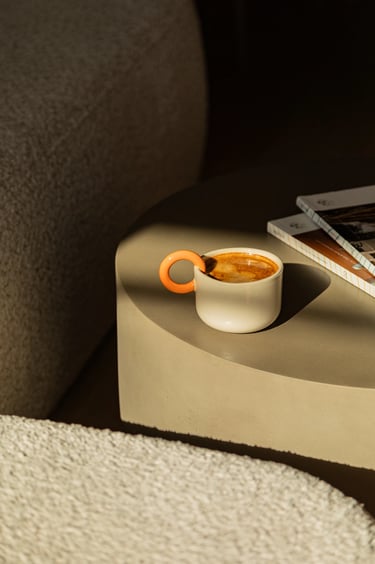 Designerski kubek z kawą na stoliku kawowym w promieniach słońca.