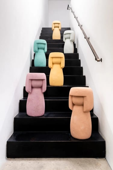 Mehrere bunte Kokeshis aus Stein stehen auf einer Treppe und schauen nach unten