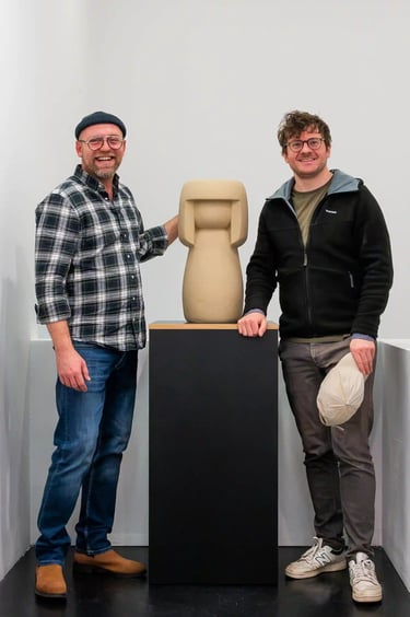 Richard und Felix stehen neben einer Kokeshi, die auf einem Podest steht