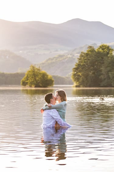 un couple enlacé dans un lac avec des montagnes en arrière plan au coucher du soleil
