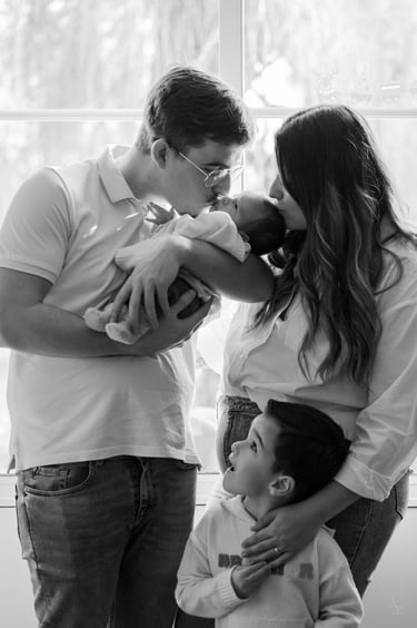 une famille de quatre personnes debout devant une fenêtre avec un bébé dans les bras