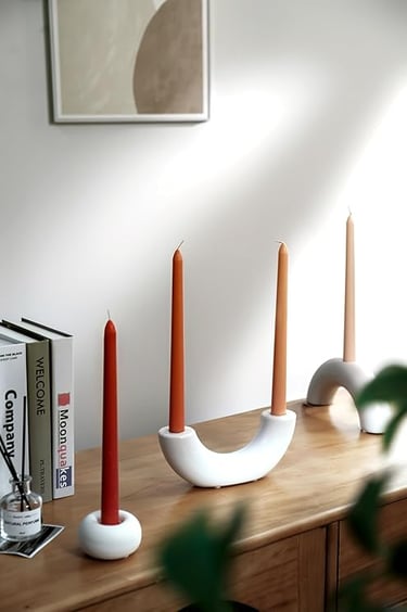 Modern white ceramic candle holders with burnt orange taper candles on wooden console table