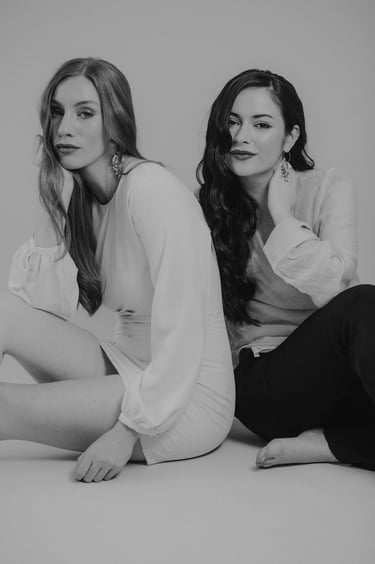 two women sitting on the floor in front of a white wall