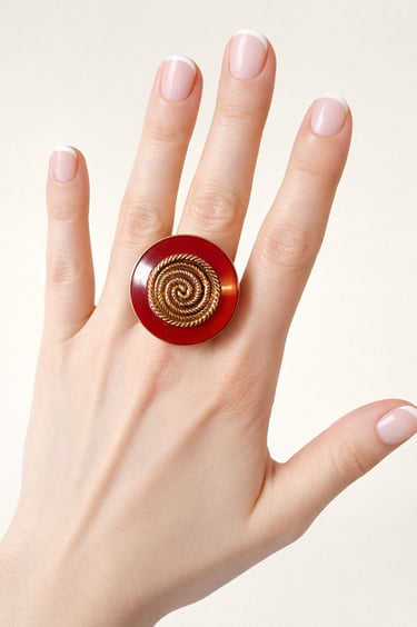 Vintage statement ring with a large red circular base and gold spiral design on a hand.
