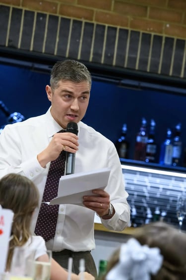 A man in a white shirt and tie gives a formal speech with a microphone and notes at an event.