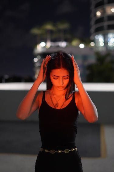 Young woman in a black tank top posing at night on a rooftop with city lights bokeh.
