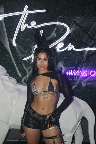 Woman in a black bunny costume and sequin bikini top poses at a Halloween party.