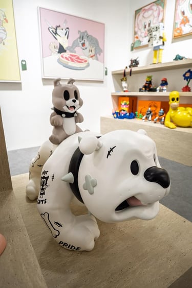 A vinyl designer toy of a cartoon mouse riding a bulldog statue in a modern art gallery exhibit.