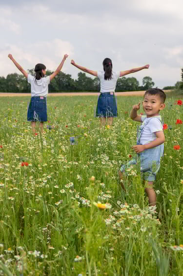 Young boy playing in a wildflower meadow with girls standing with arms raised in the background.