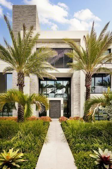 Modern luxury home exterior with stone accents, palm trees, and a white stone walkway.