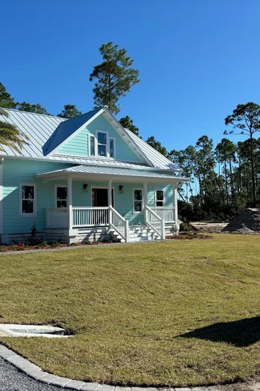 New light blue coastal home with a metal roof, front porch, and palm tree on a grassy lawn.