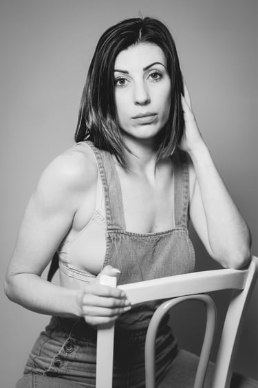 Portrait en noir et blanc d’une femme assise sur une chaise, en salopette, le regard franc.