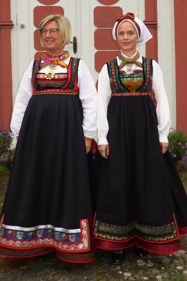 Two women stand in front of a building in empire waisted bunad
