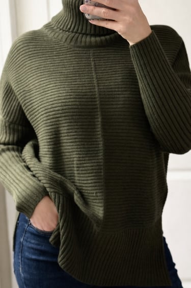 Close up of an army green ribbed turtleneck sweater styled with jeans for a casual outfit