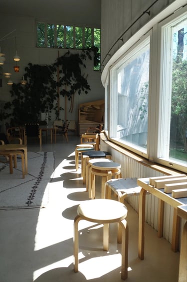 Alvar Aalto Studio room with wooden stools, soft sunlight and large windows overlooking nature