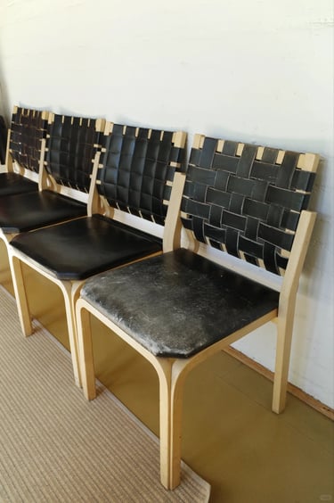 Pair of wooden chairs with black woven seats, reflecting Alvar Aalto’s practical furniture design