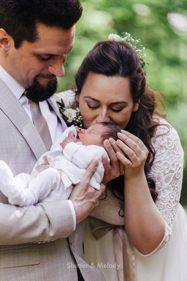 Bride kissing her baby's head while groom holds it.
